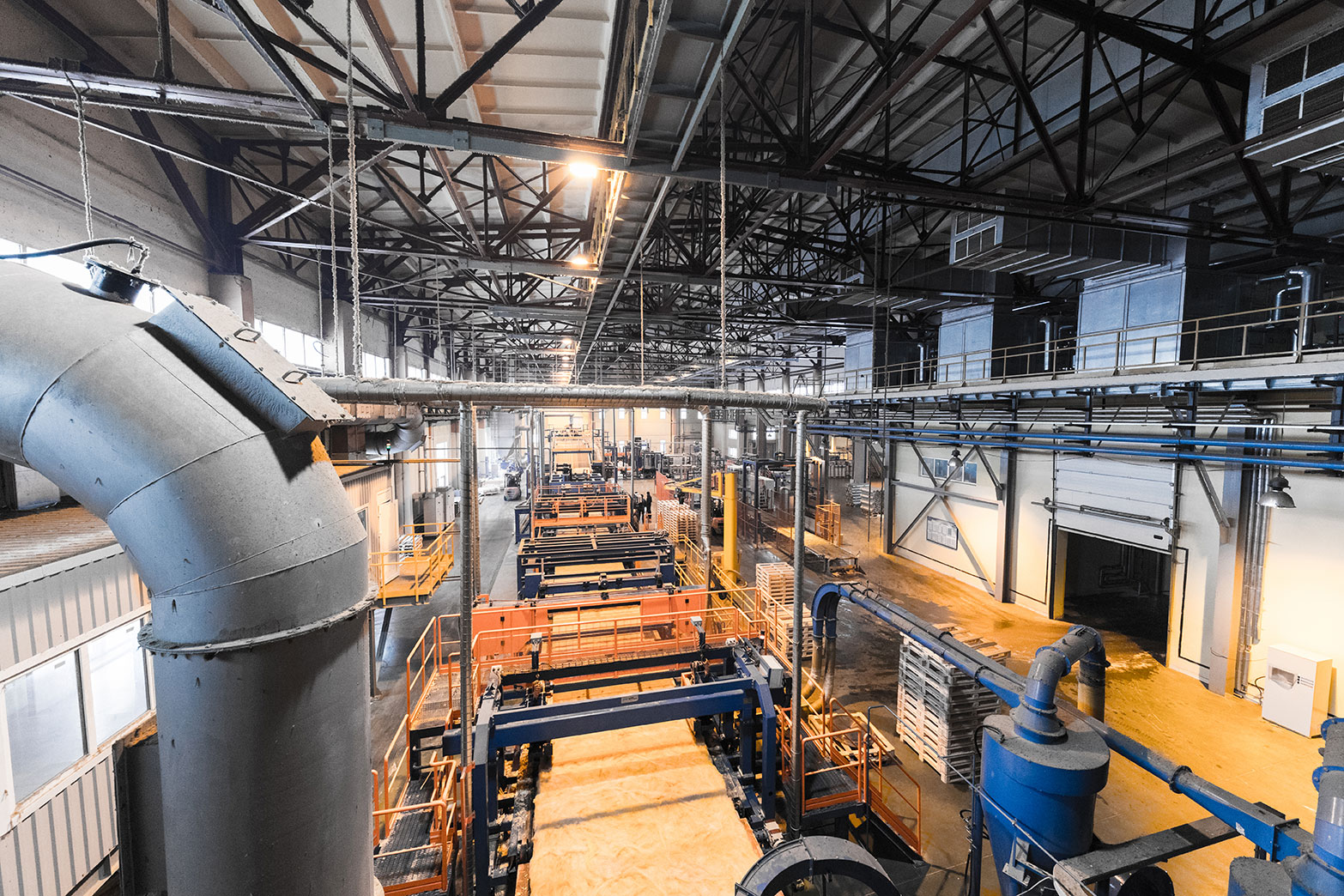 Heavy industrial processing plant — overhead conveyors, lifts, and structural steel above a process line.